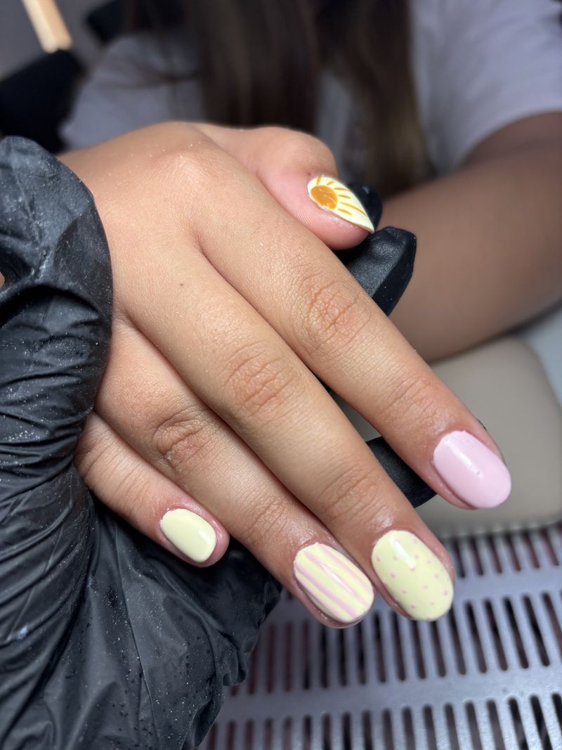 Unhas em amarelo e rosa pastel com riscas e um sol pintado à mão